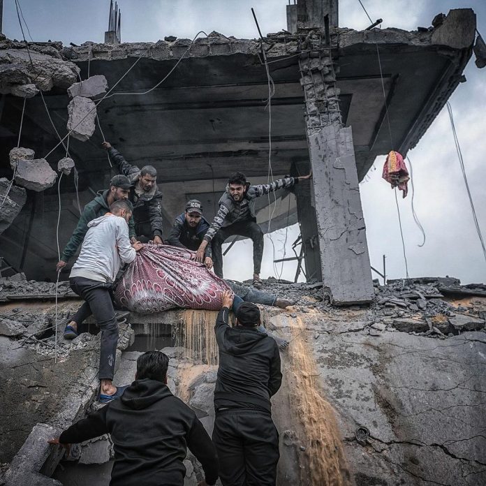 Palestinians trying to evacuate a woman body after she passed in a building that got bombed by the Israeli war planes. Credit: Motaz Azaiza